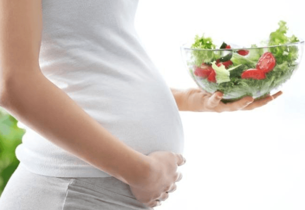 Беременная держит миску с овощами